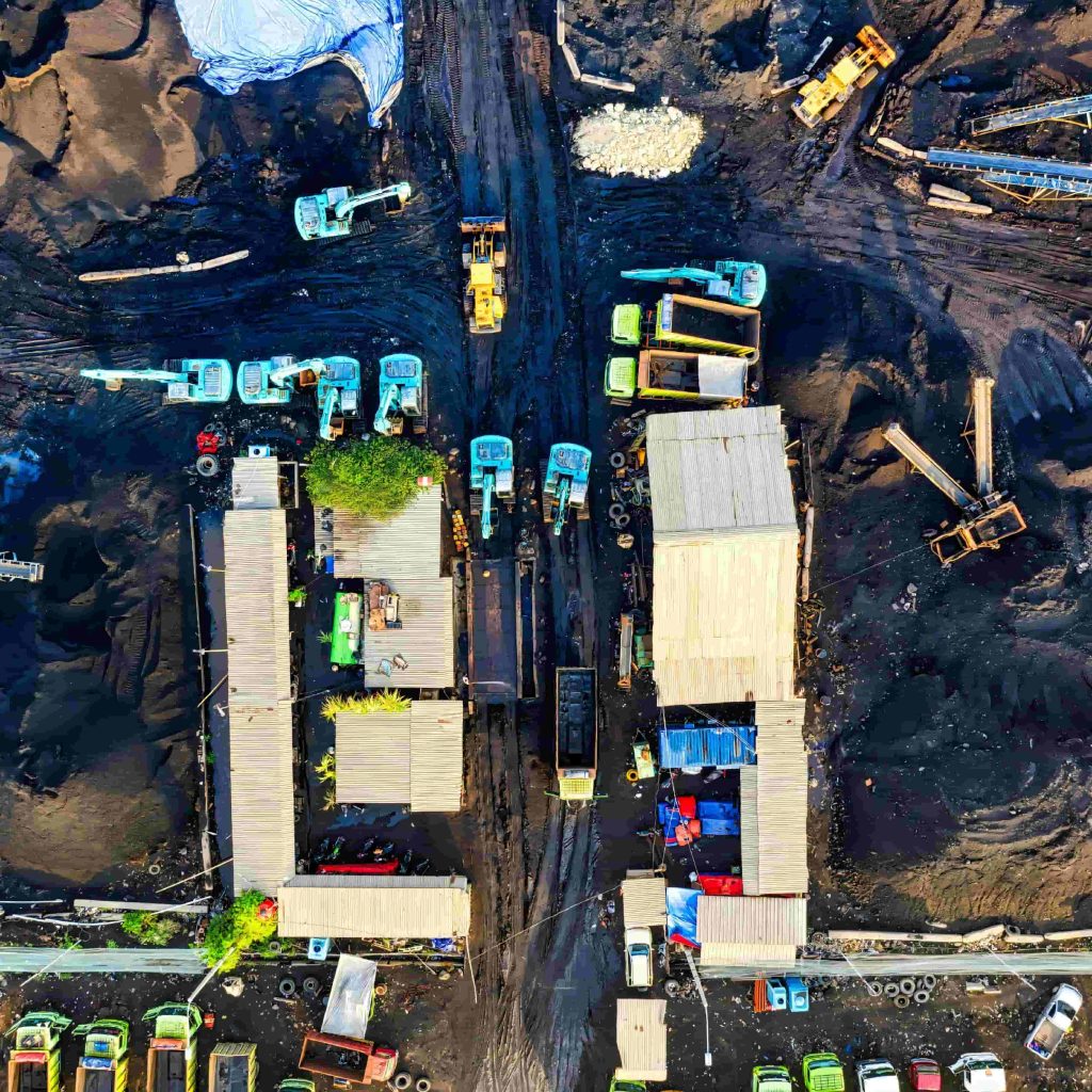Top-down aerial view of a bustling mining site in Rustenburg with excavators, dump trucks, and facility rooftops surrounded by dark earth, representing a heavy industrial site powered by a MegSolid BESS.