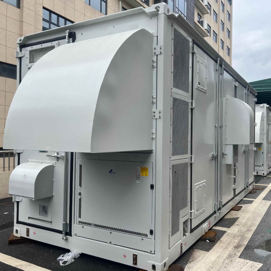 A large, white industrial container for energy storage resting on outdoor pavement, equipped with heavy-duty locking doors, external cooling hoods, and visible safety grounding points.