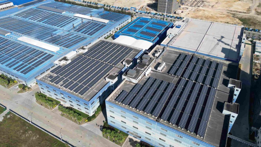 High-altitude drone shot of an expansive blue industrial manufacturing complex in Sydney, featuring dense rows of rooftop photovoltaic (PV) panels paired with a MegSolid commercial energy storage system.