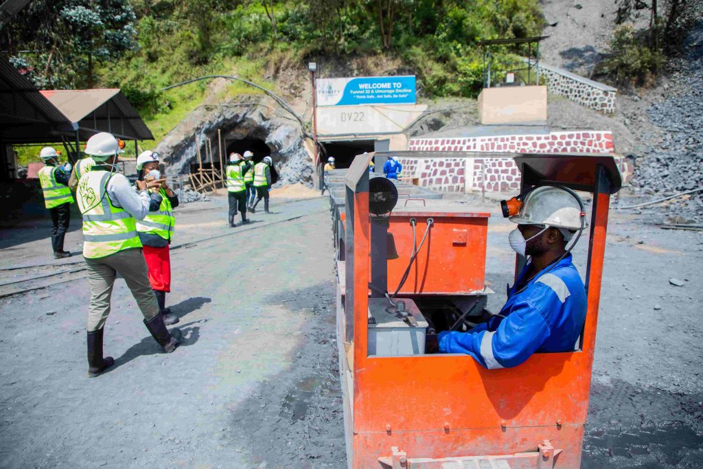Mining crew in high-visibility vests and hard hats gathered near a tunnel entrance, with a worker operating an orange mine cart in the foreground, supported by MegSolid backup power systems.